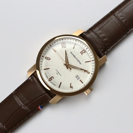 Montre Humbert Droz HD8 au style intemporel or rose, cadran blanc et bracelet en cuir marron.